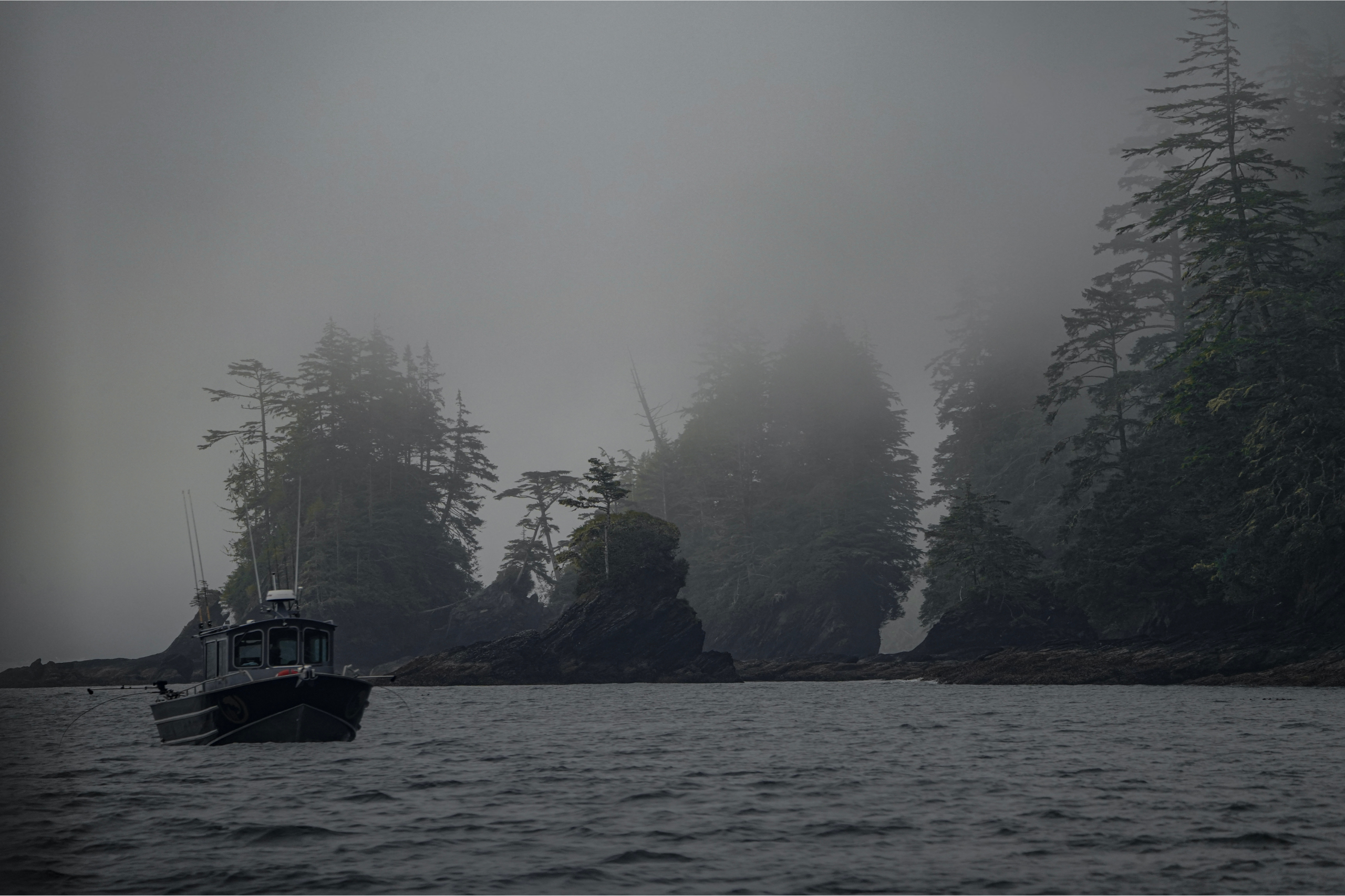 A fishing boat floats in front of foggy rock formations.